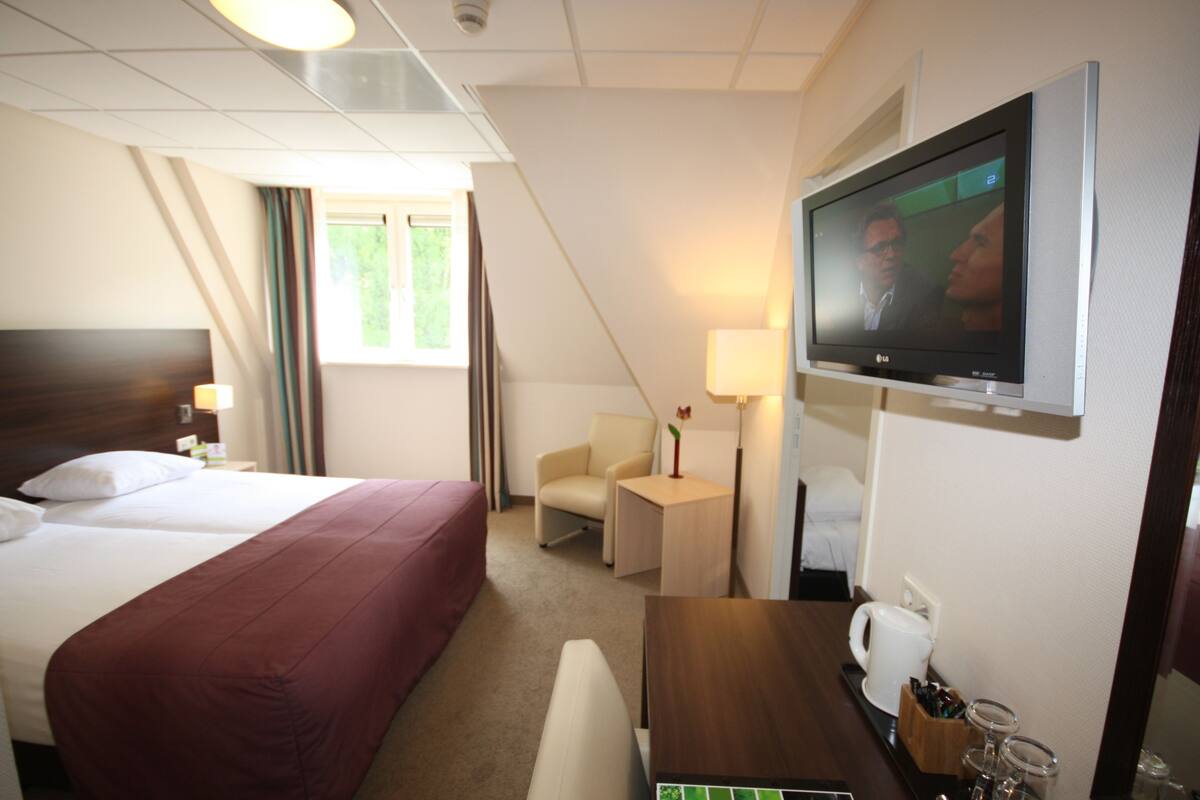 A hotel room with a large bed, a desk, a chair, a television, and a window with curtains.