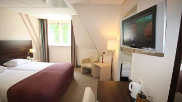 Hotelkamer met een groot bed, een bureau, een stoel, een televisie en een raam met gordijnen.