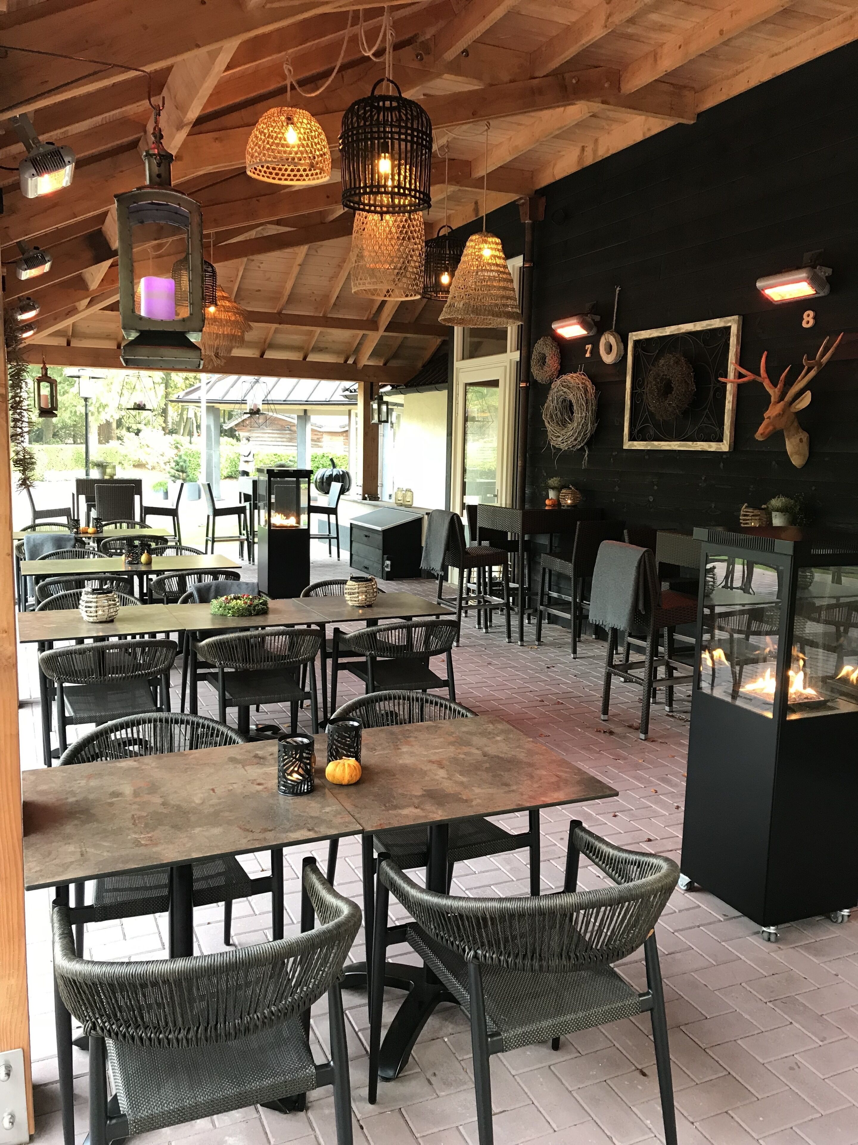 Un espace de restauration extérieur de style rustique, avec des chaises et des tables en osier, des poutres en bois et des luminaires suspendus.
