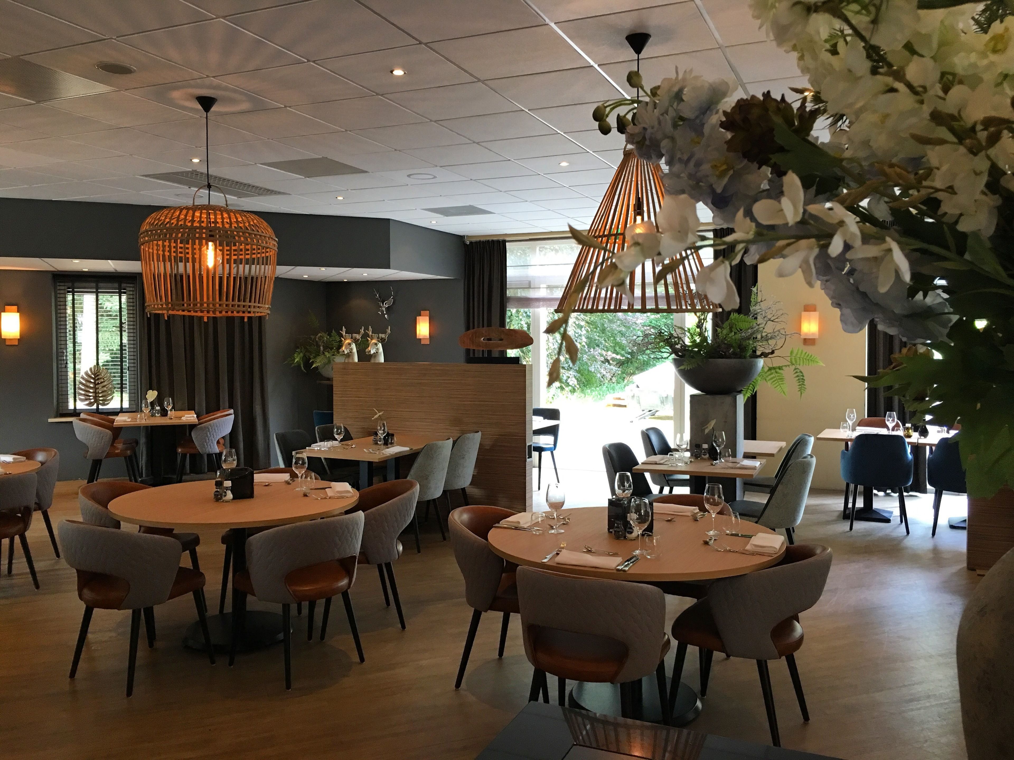 Un'area pranzo moderna con tavoli rotondi, sedie imbottite e lampade a sospensione.