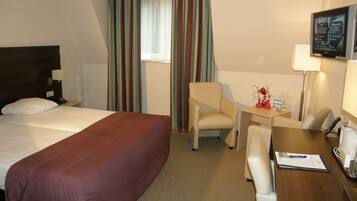 A hotel room with a bed, a desk, a chair, a TV, and curtains.