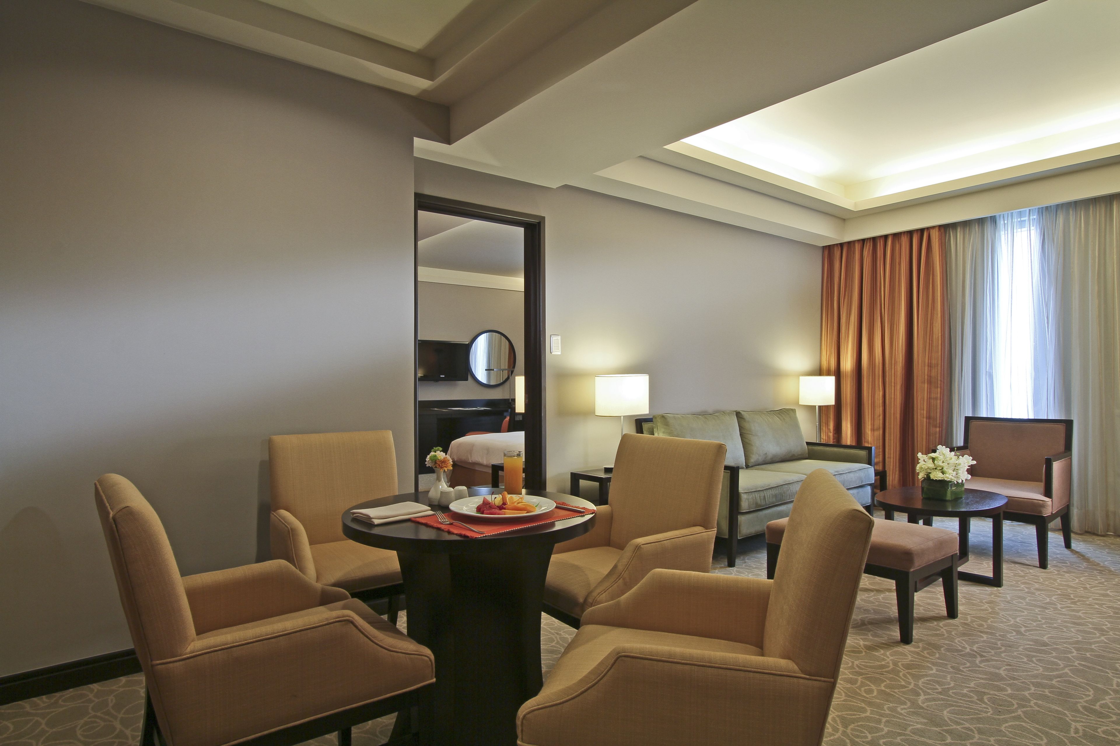 Habitación de hotel con zona de comedor, sofá, mesa de centro y vistas al exterior.