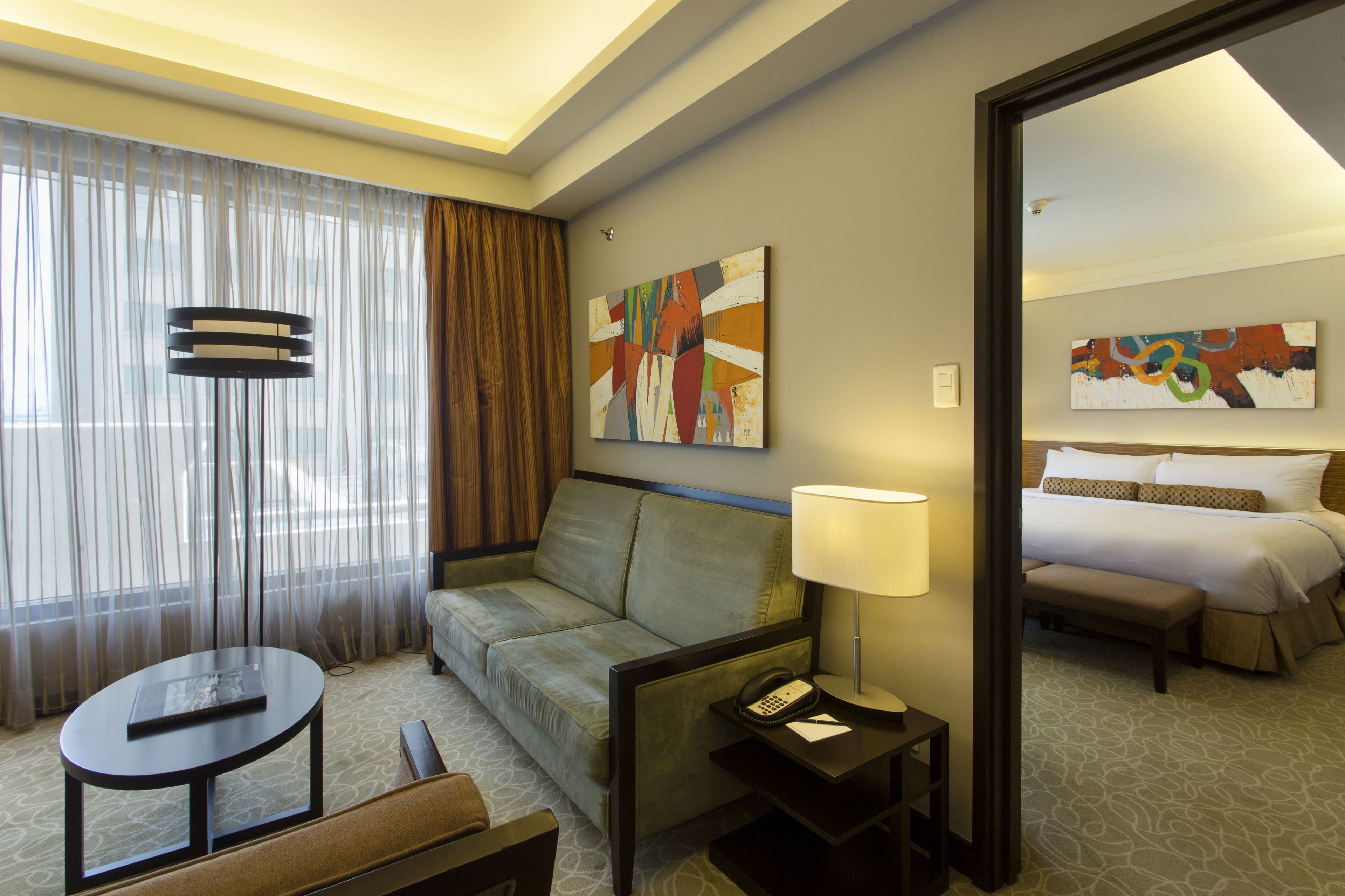 A hotel room with a sofa, a small table, a lamp, a telephone, and a painting on the wall.