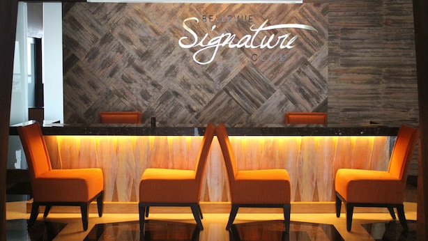 A reception area with a herringbone wood panel wall, a reception desk, and two orange chairs. - The Bellevue Manila  (Muntinlupa)