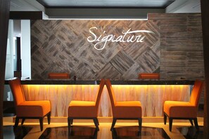A reception area with a herringbone wood panel wall, a reception desk, and two orange chairs. - The Bellevue Manila  (Muntinlupa)