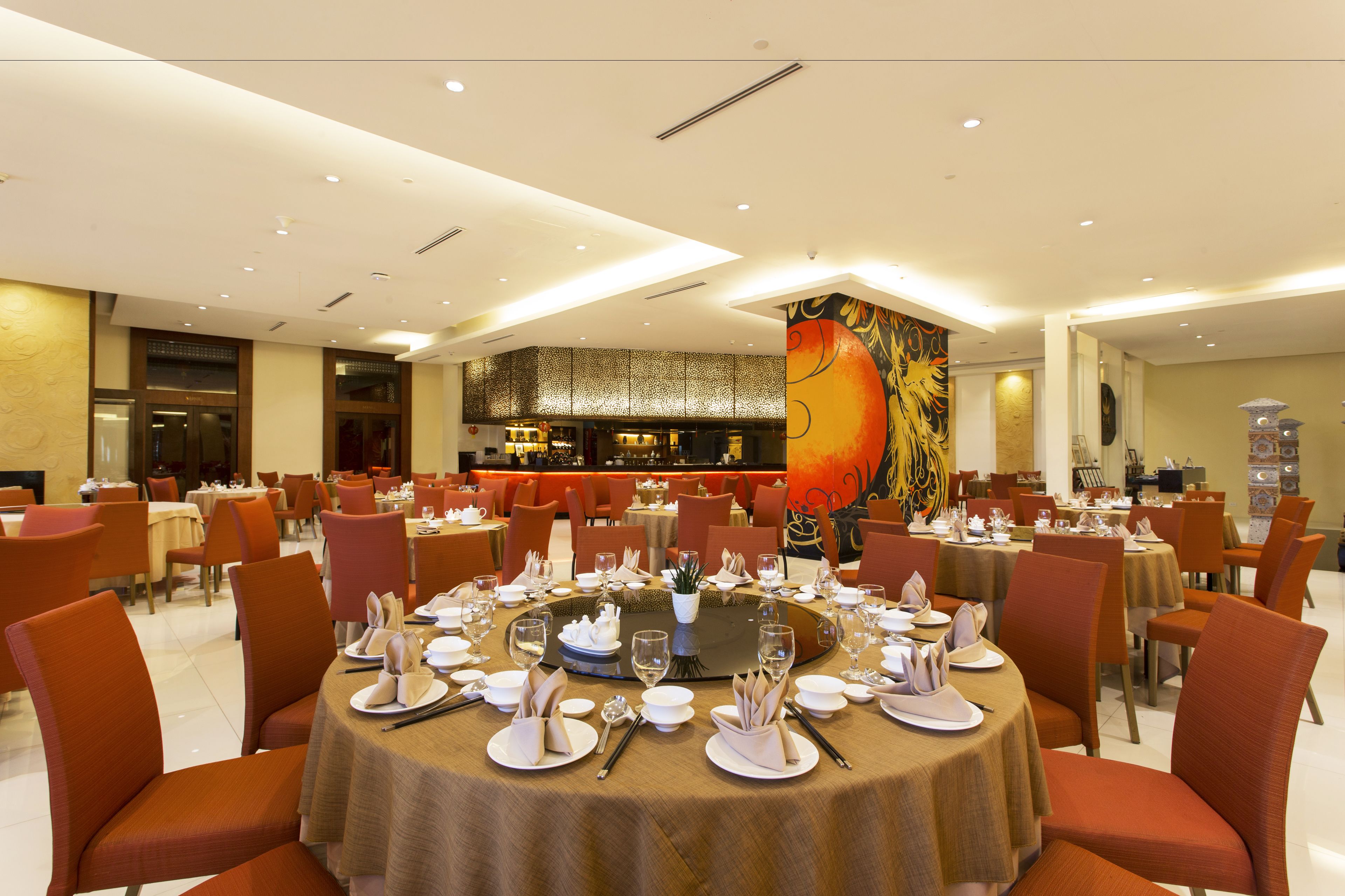 A restaurant with round tables set for dining, orange chairs, and a large mural on the wall.