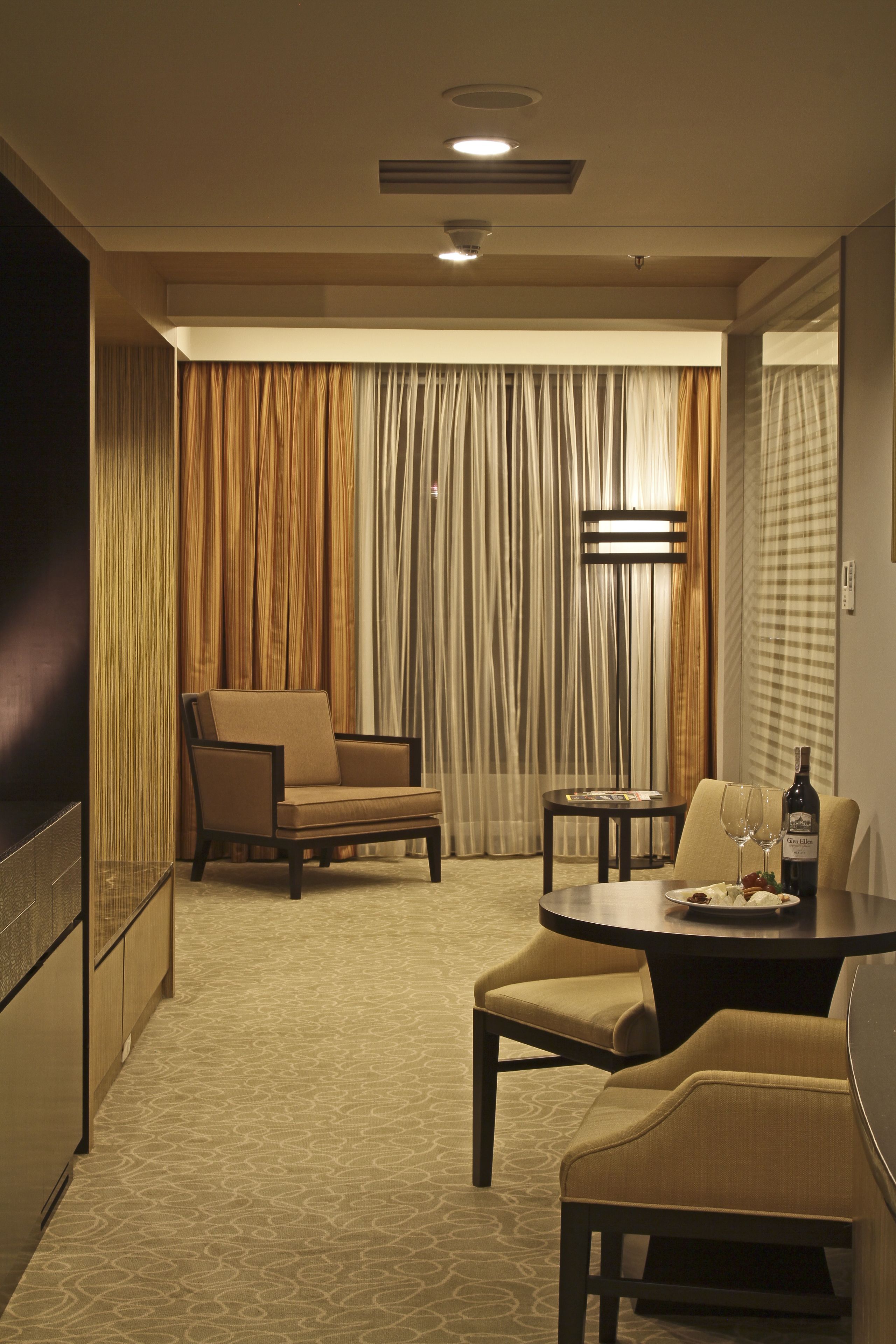 A hotel room with a dining area featuring a table, chairs, and a bottle of wine.