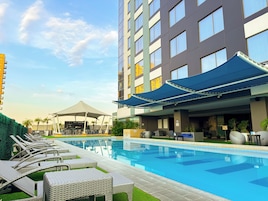 Zona de piscina de hotel con sillones reclinables y un edificio grande con varias ventanas.