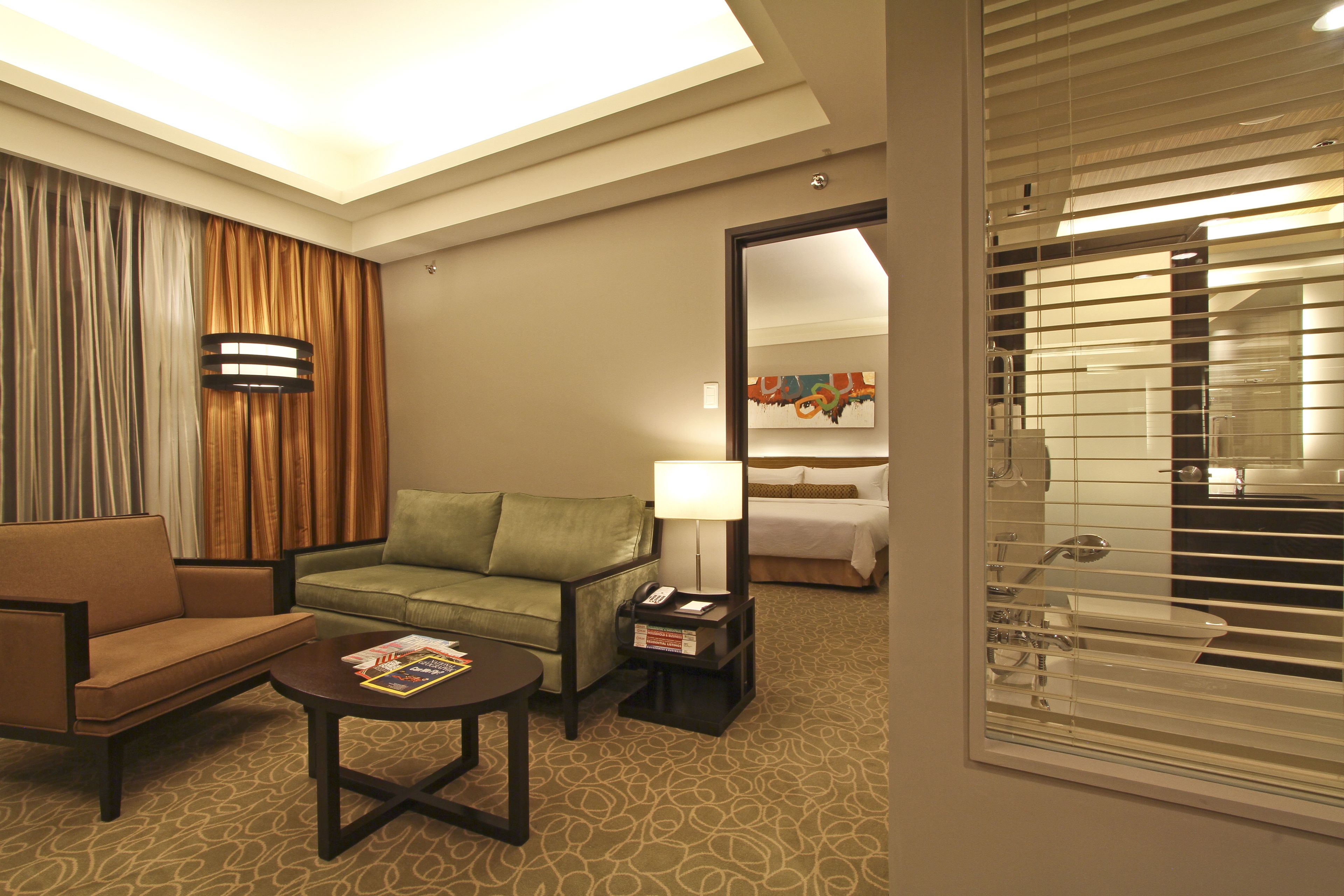 A hotel room with a sofa, a small table with a magazine, a lamp, and a nightstand with a phone.