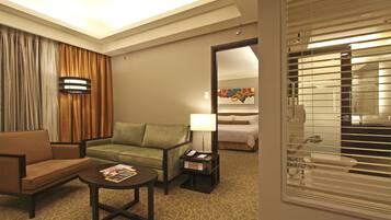 A hotel room with a sofa, a small table with a magazine, a lamp, and a nightstand with a phone.