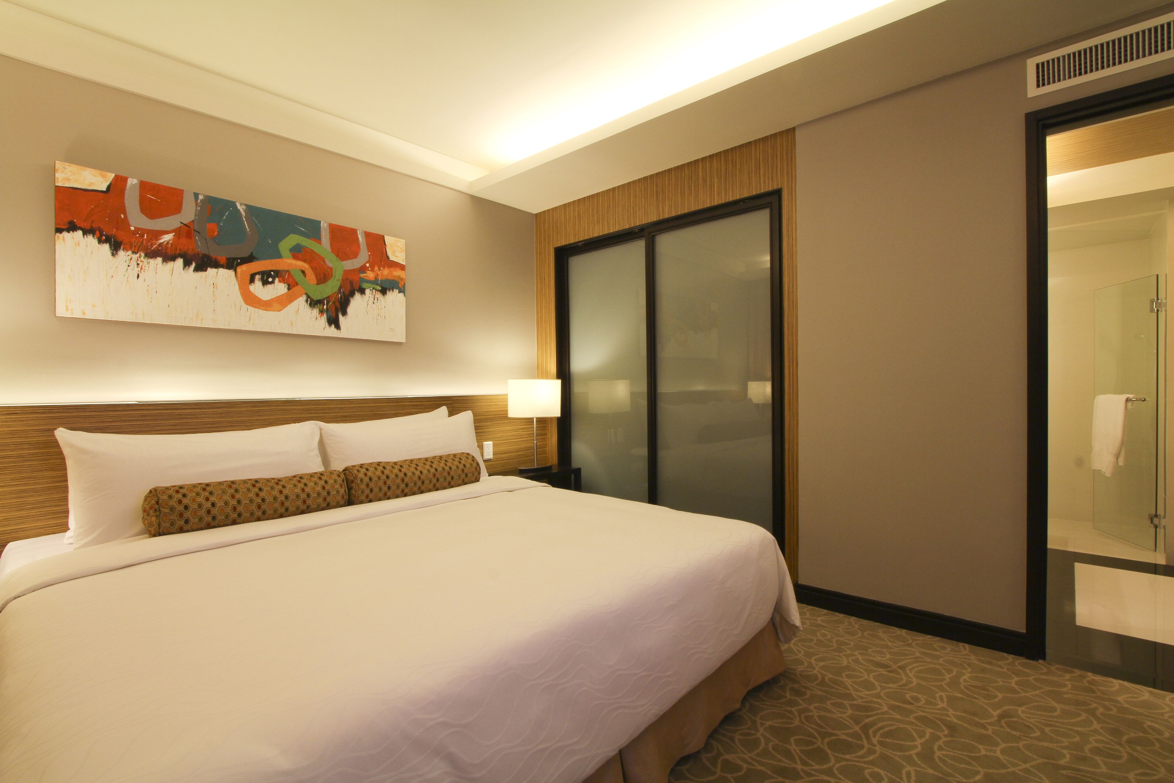 A hotel room with a large bed, a painting on the wall, a sliding door, and a carpeted floor.
