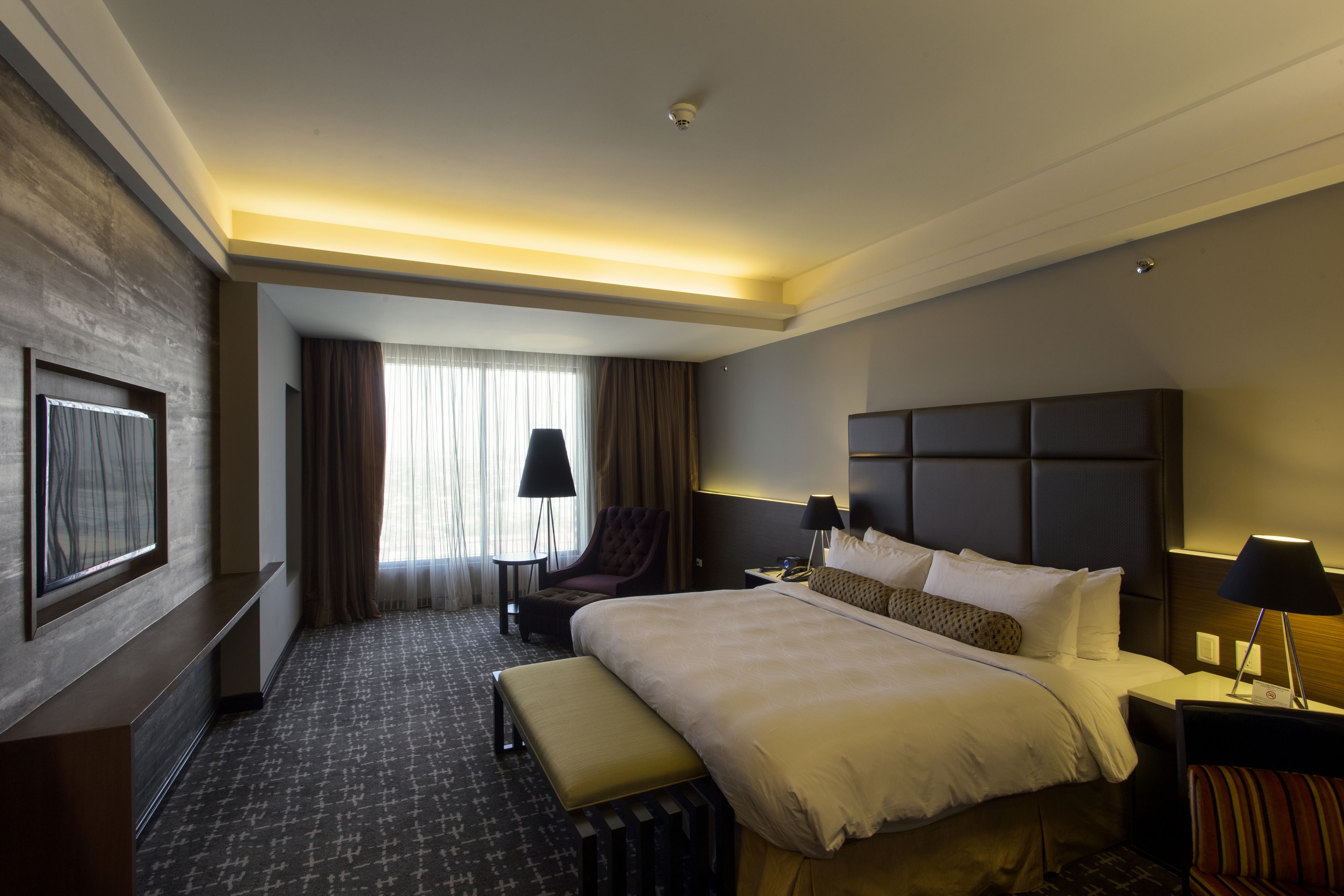 Une chambre d’hôtel avec un grand lit, un bureau, une chaise, un banc et une vue sur l’extérieur par une fenêtre.