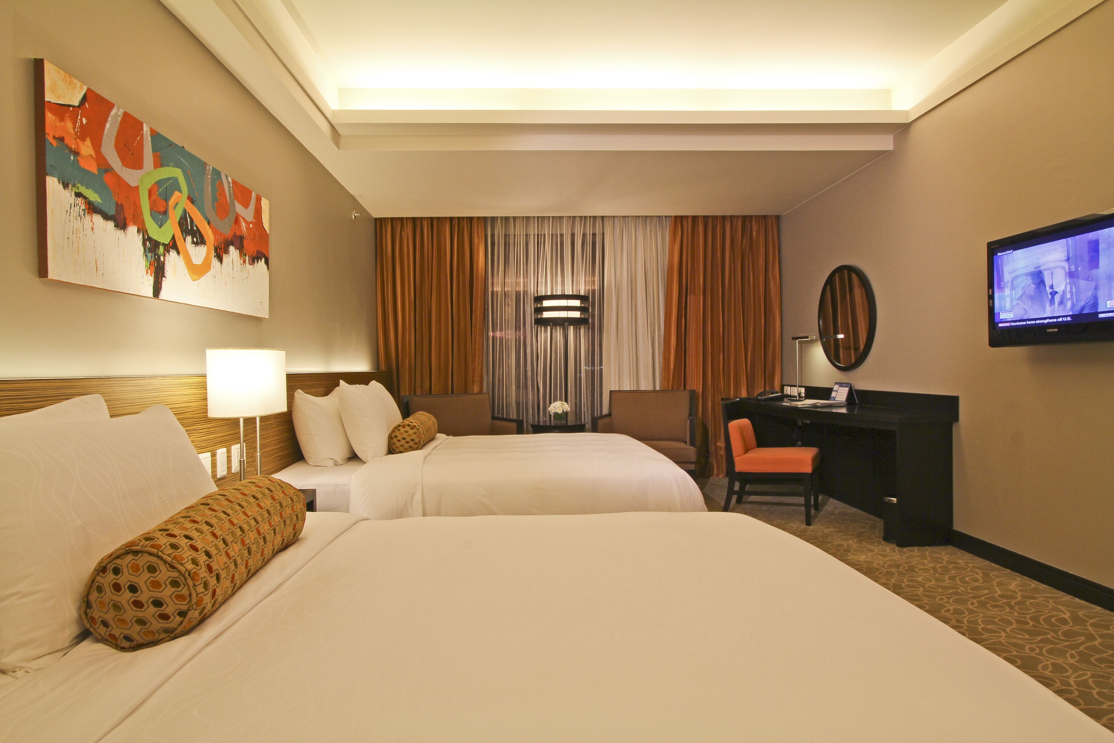 A hotel room with two beds, a desk, a TV, and a painting on the wall.