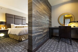 Habitación de hotel con cama, mesita de noche, lámpara, escritorio, silla y un espejo grande.