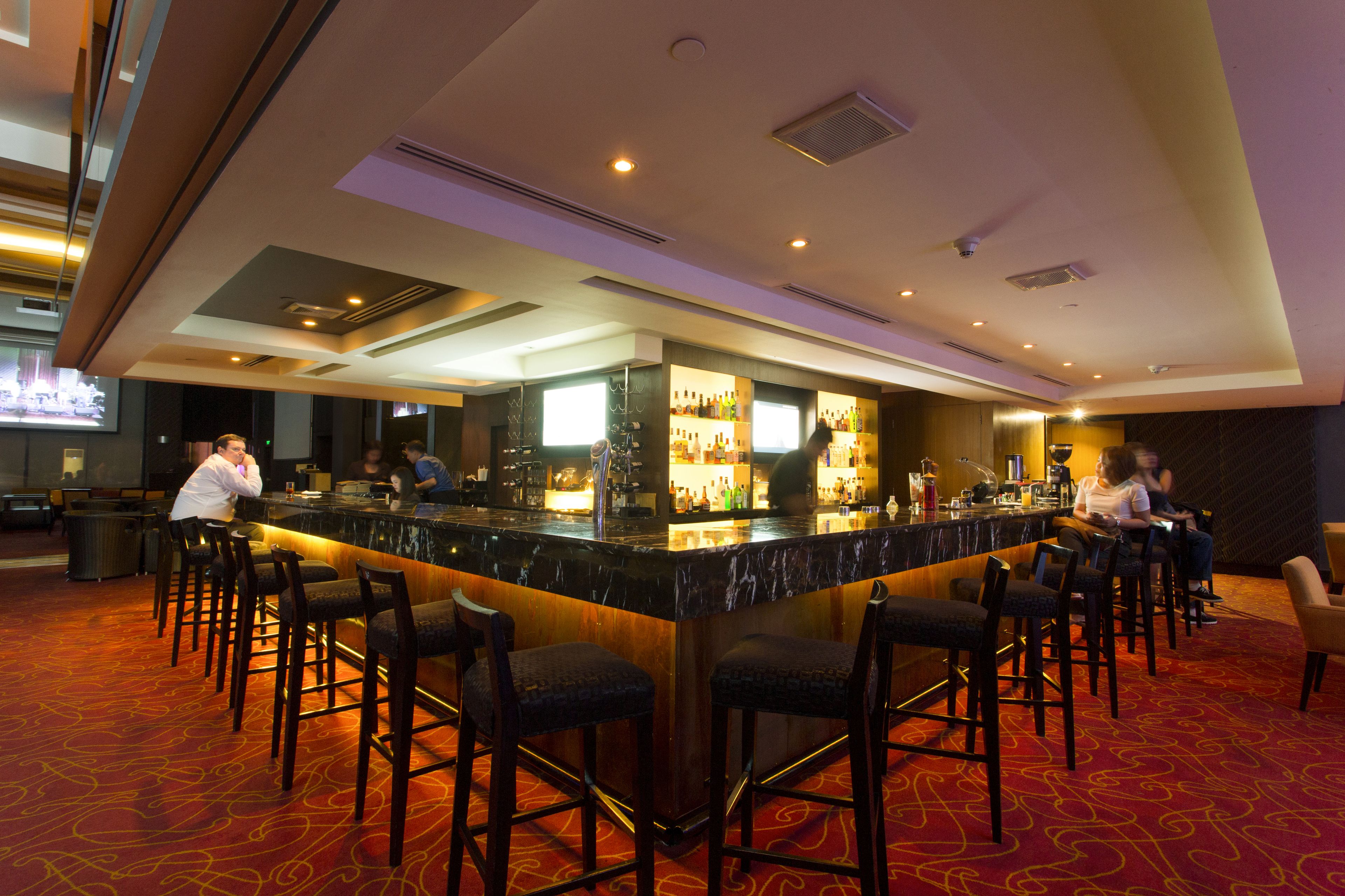 A bar area with a marble countertop, multiple bar stools, and a red carpeted floor.