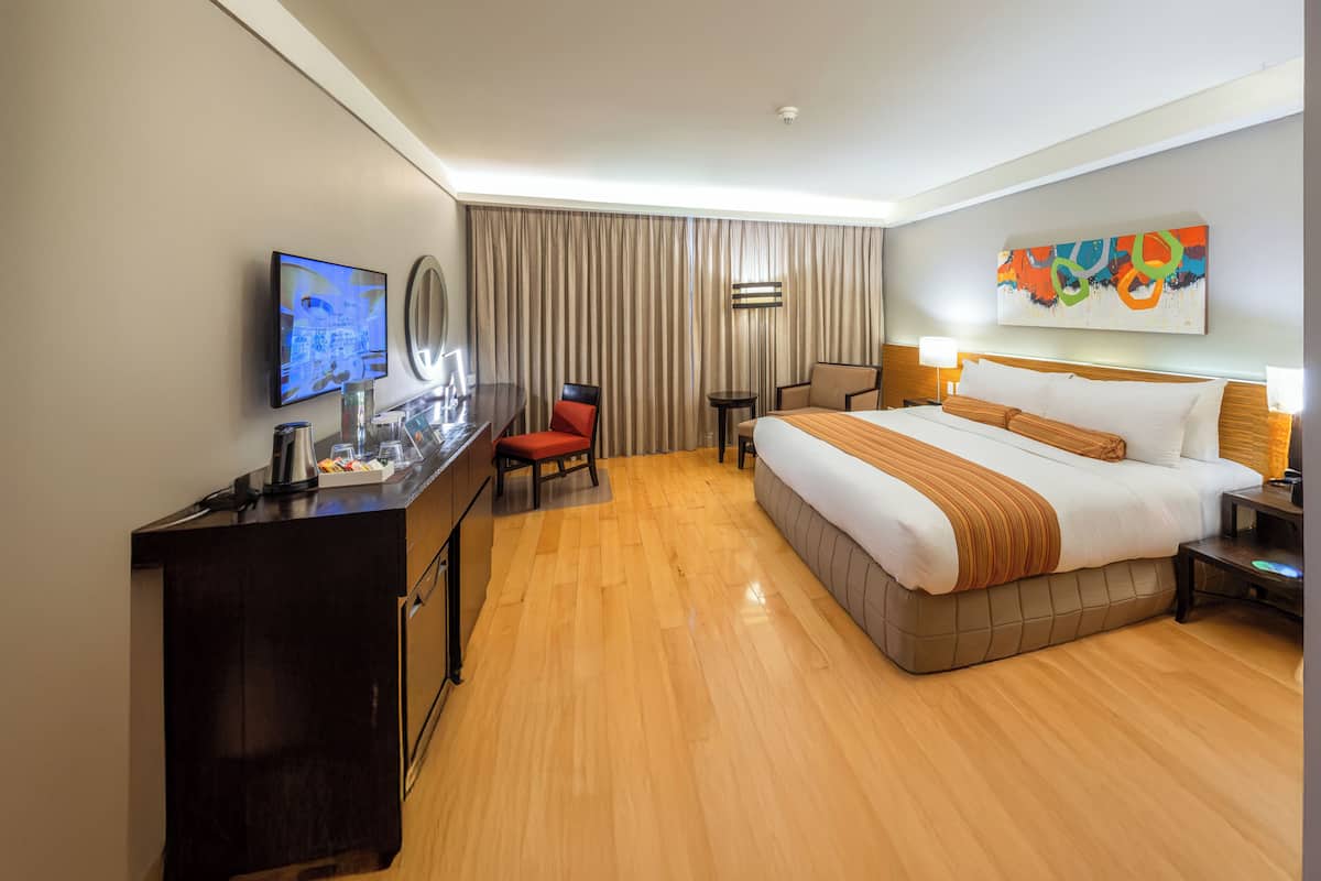 A hotel room with a large bed, a desk with a TV, a chair, and a small table.