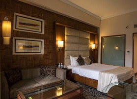 A hotel room with a bed, a sofa, a glass coffee table, and two wall-mounted lamps.