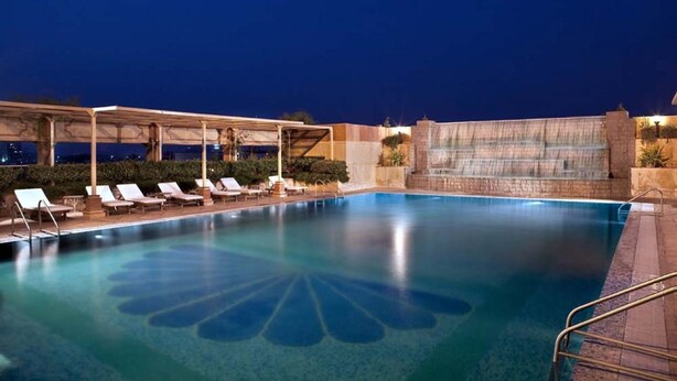 Piscina à noite com água cristalina, espreguiçadeiras e área coberta com um elemento aquático.