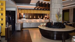 Um hall de hotel moderno com uma recepção central, uma escadaria e uma área de estar.