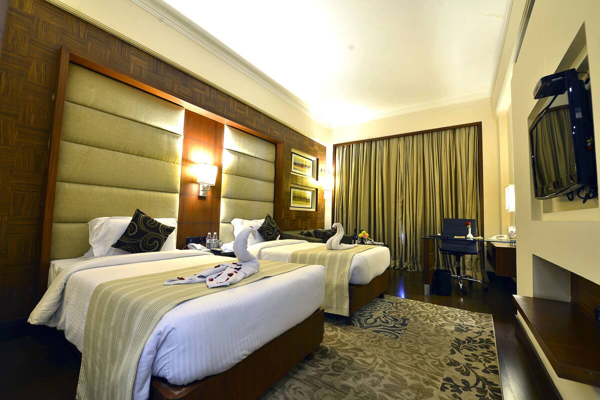 A hotel room with two beds, a desk, a chair, a television, and a window with curtains.