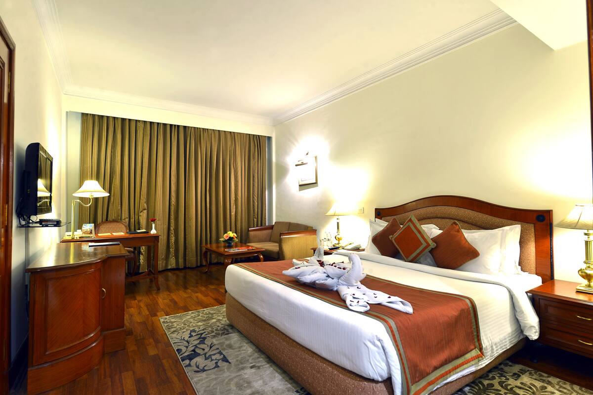 A hotel room with a large bed, a desk, a chair, a TV, and a window with curtains.