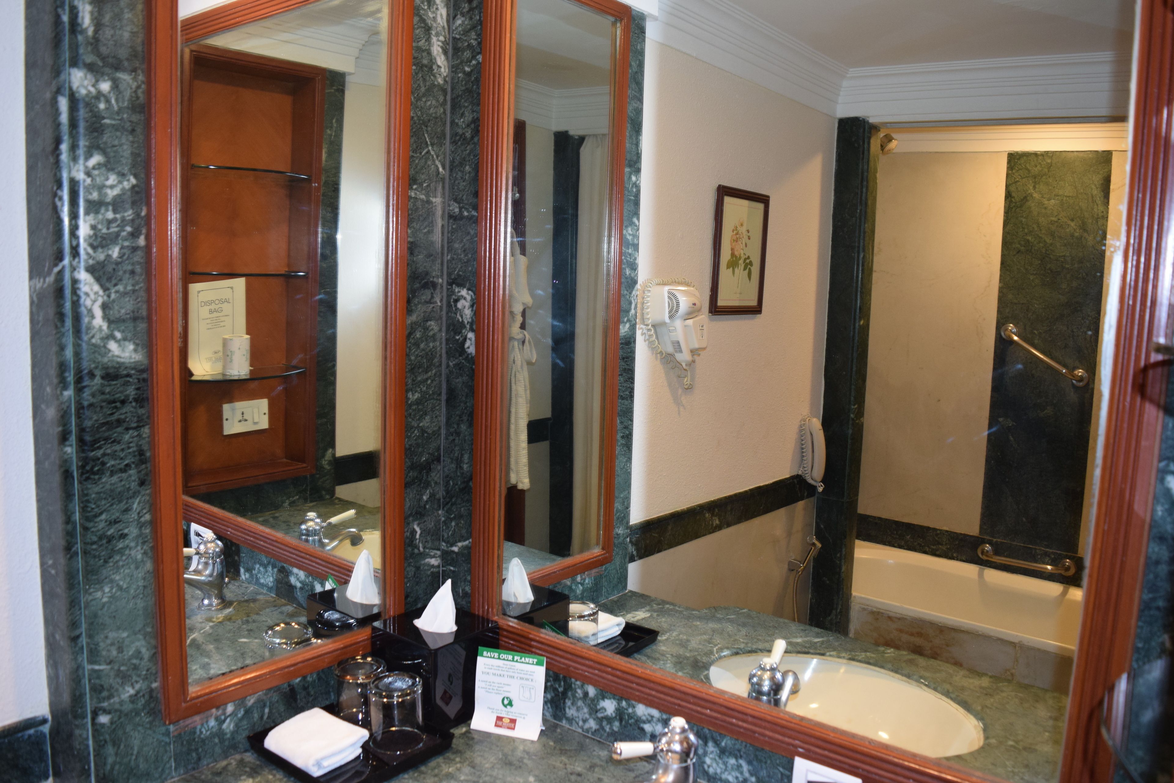 Une salle de bain avec un lavabo en marbre, un grand miroir, un porte-serviettes, un sèche-cheveux et un espace douche.