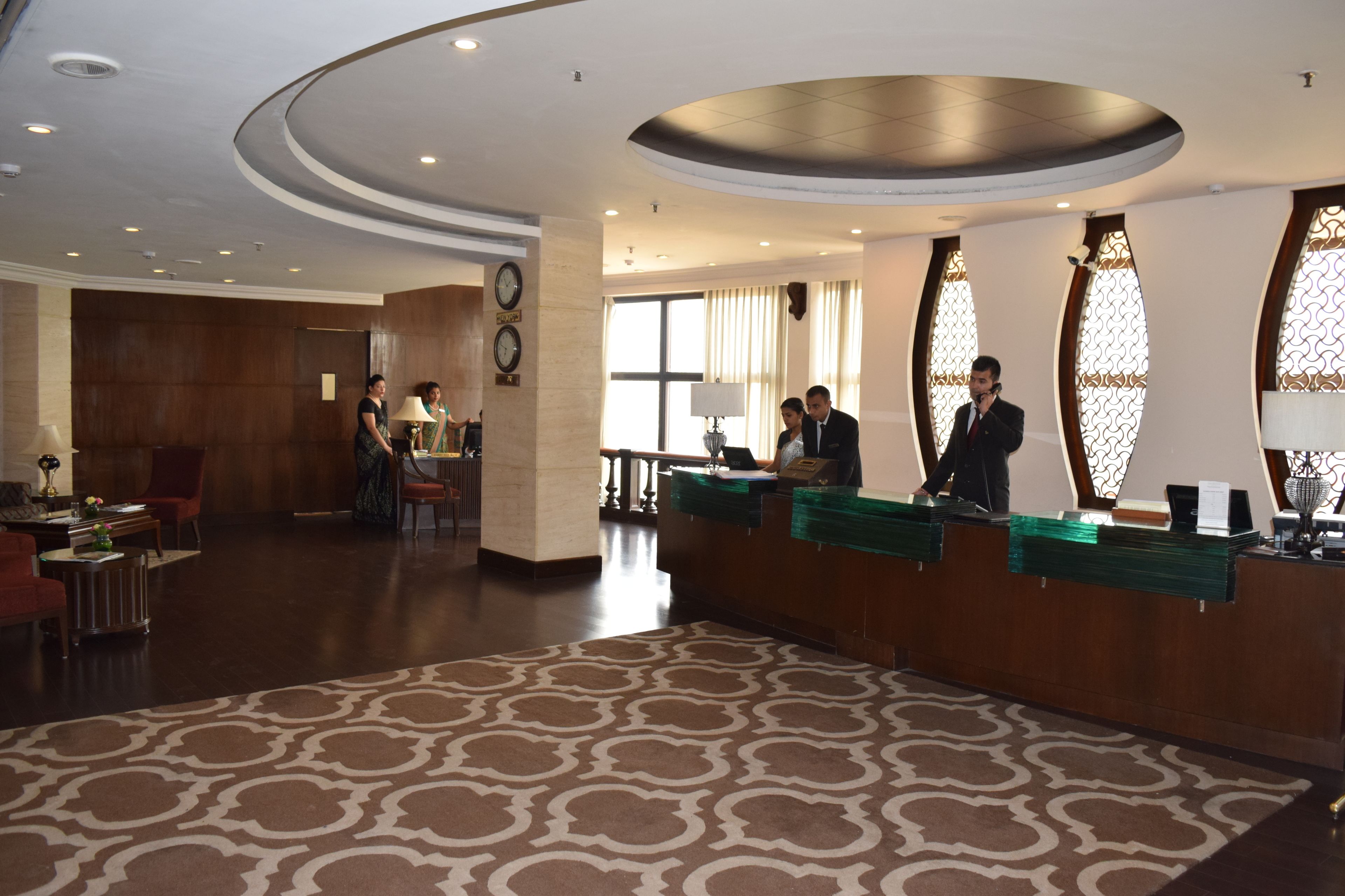 Een hotel receptie met een kamerbreed tapijt, een houten receptiebalie en grote ramen met decoratief glas.