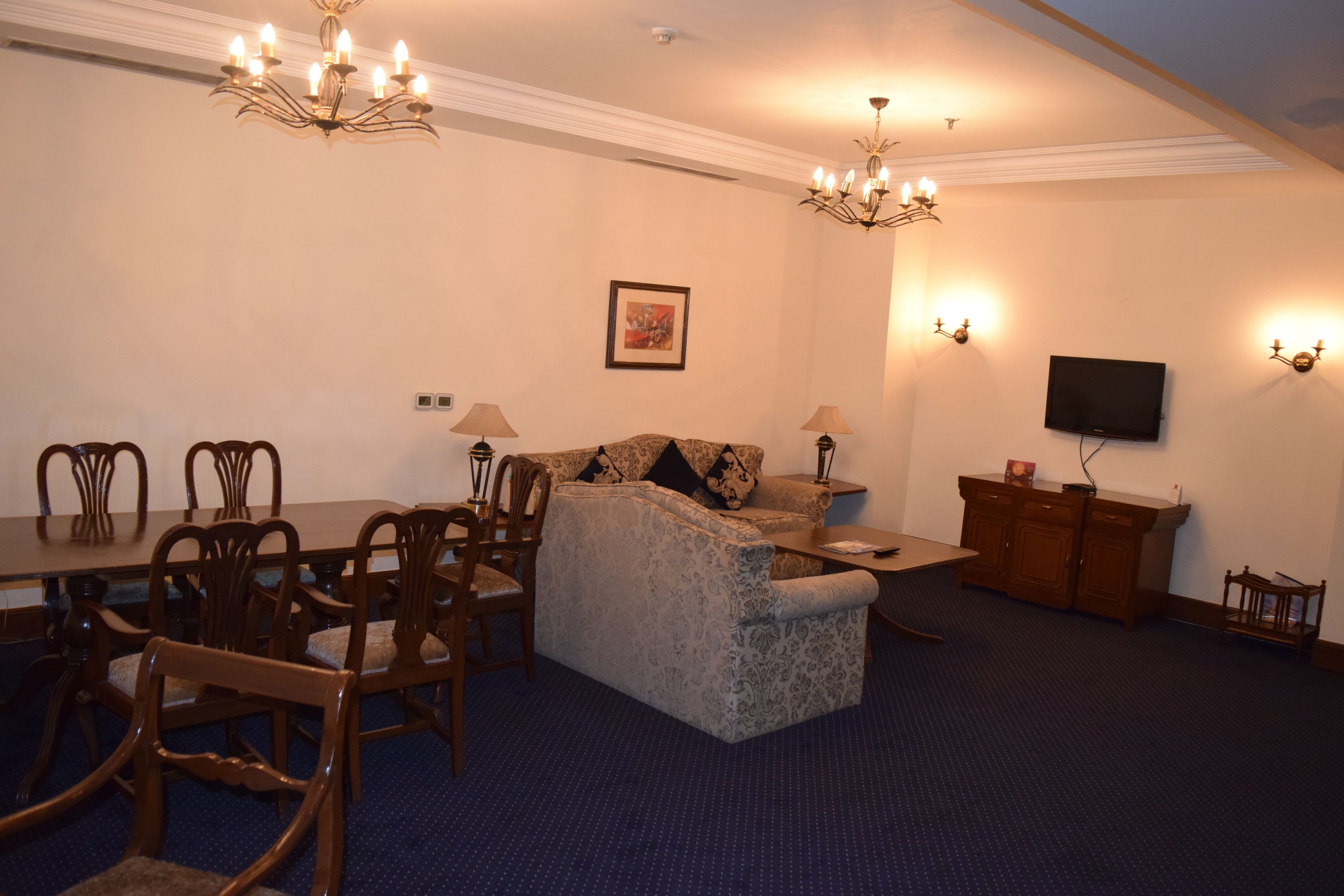 A dining area with a long table and chairs, a sofa, and a television on a stand.
