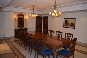 A formal dining room with a large wooden table, blue cushioned chairs, ornate ceiling light fixtures, and a framed picture on the wall.