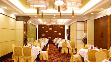Un salón de banquetes con filas de mesas y sillas, candelabros y una alfombra estampada.