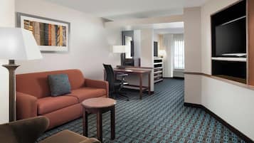 Habitación de hotel con sofá, una mesita, escritorio, silla, televisor y alfombra estampada.