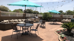 Un patio al aire libre con una mesa redonda y sillas, un sofá y dos sombrillas.