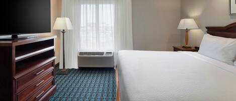 Una habitación de hotel con cama, televisión, cómoda, lámpara y aire acondicionado.