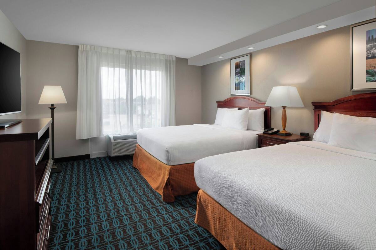 A hotel room with two beds, a desk, a chair, a TV, and a window with curtains.