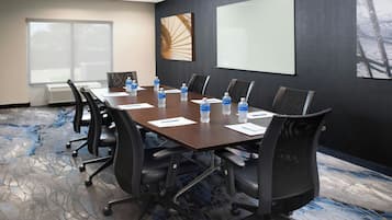 A conference room with a long table, chairs, water bottles, and a projector screen.