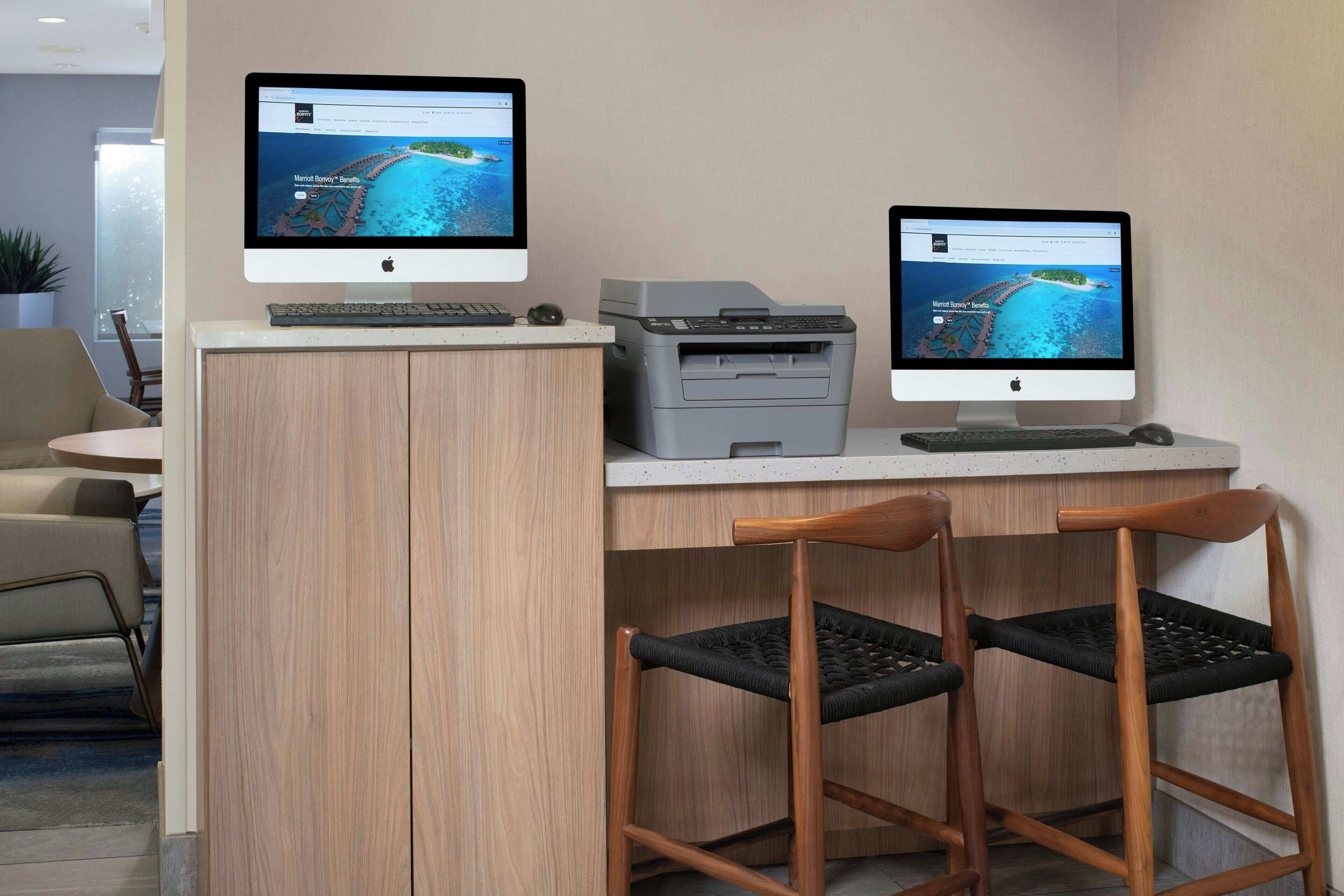 A desk with two monitors, a keyboard, a printer, and two chairs.