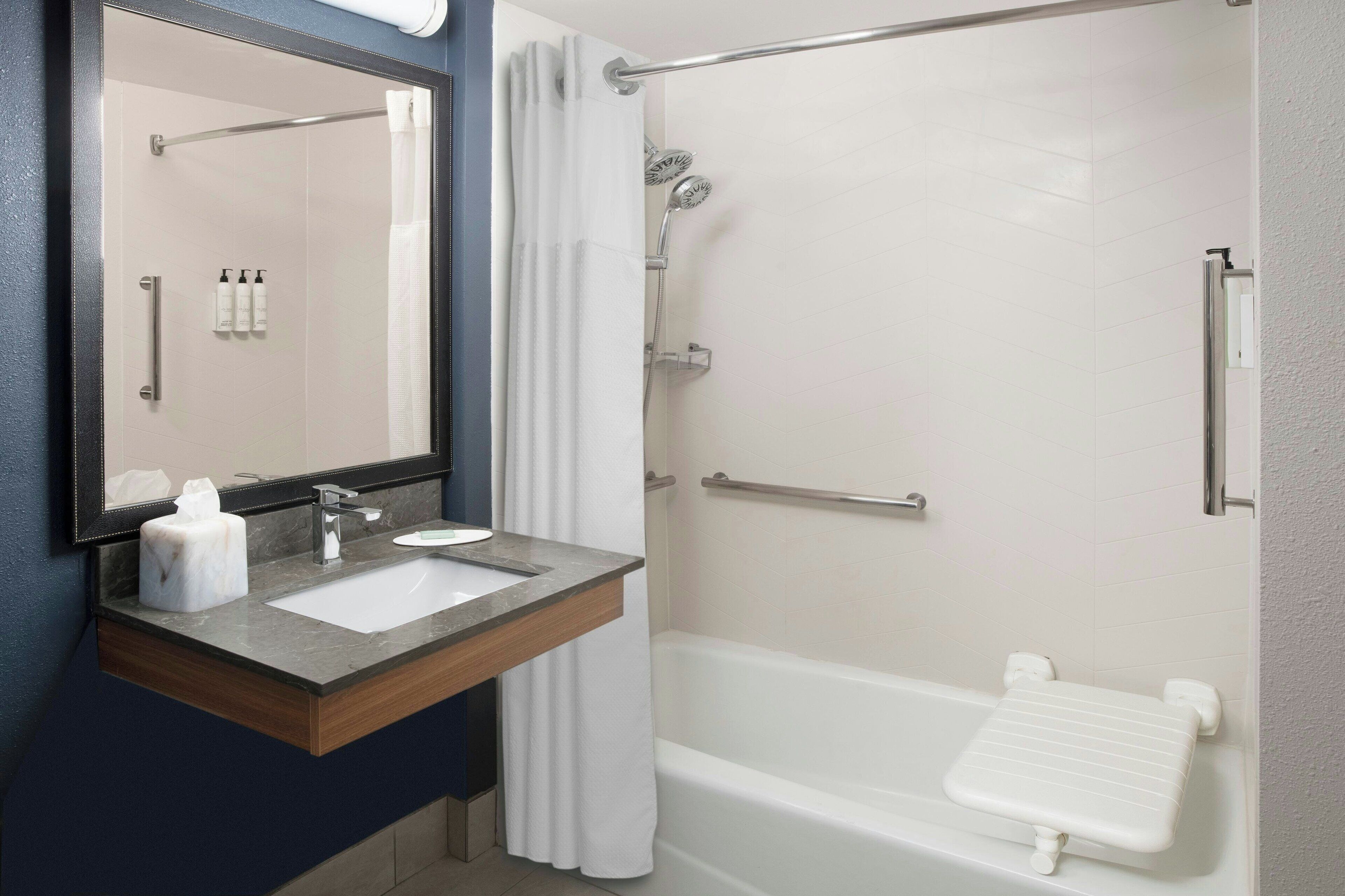 A bathroom with a sink, mirror, shower, and a towel rack.