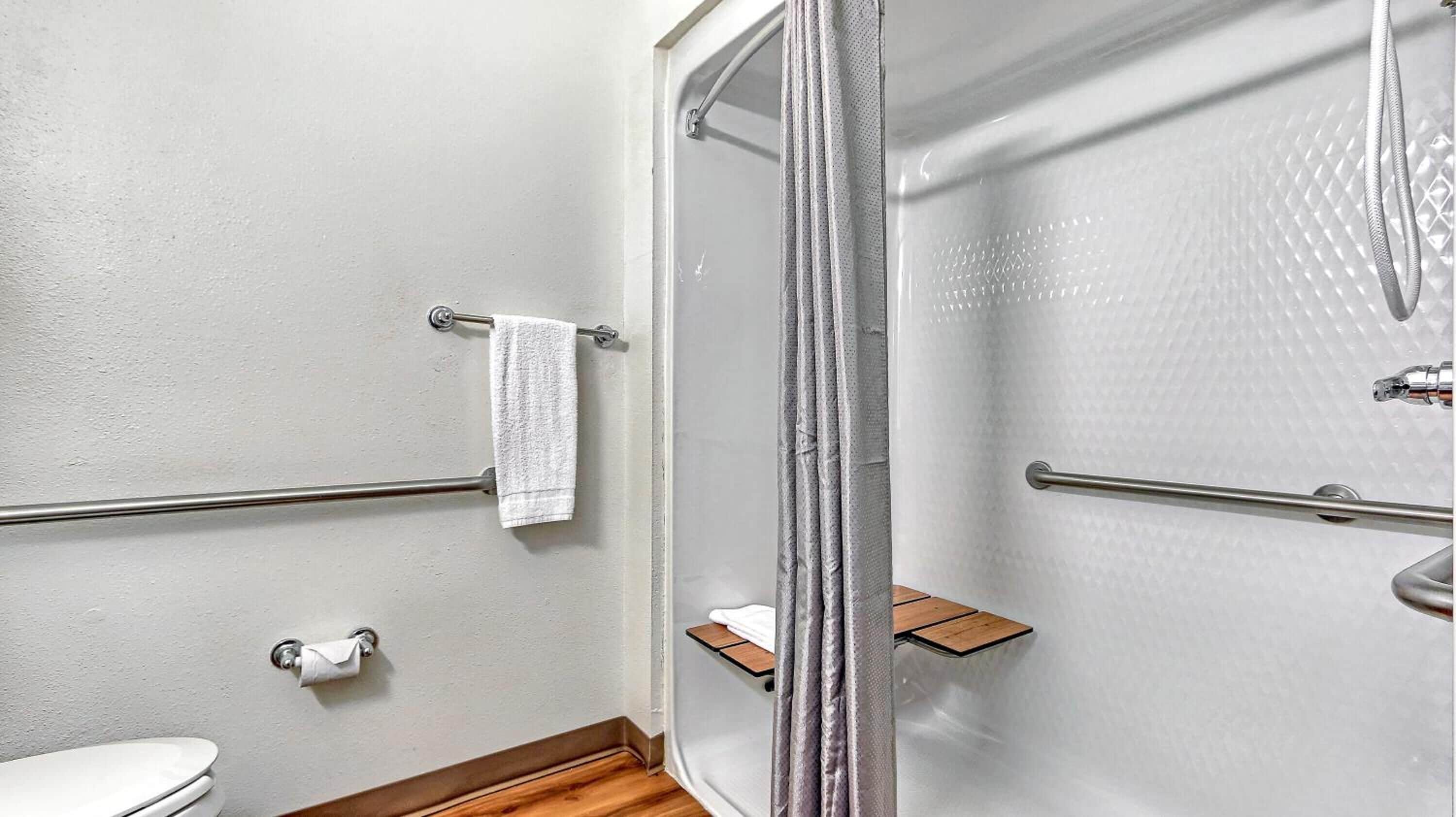 Un baño con ducha, barras de apoyo, inodoro y perchero para toallas.