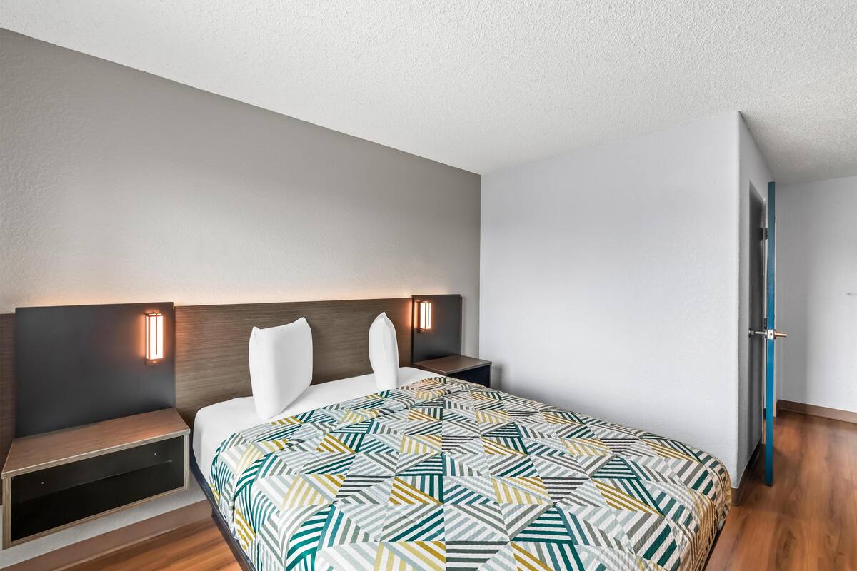 Moderni hotellihuone, jossa on suuri sänky, yöpöytä ja seinään kiinnitetty valaisin.