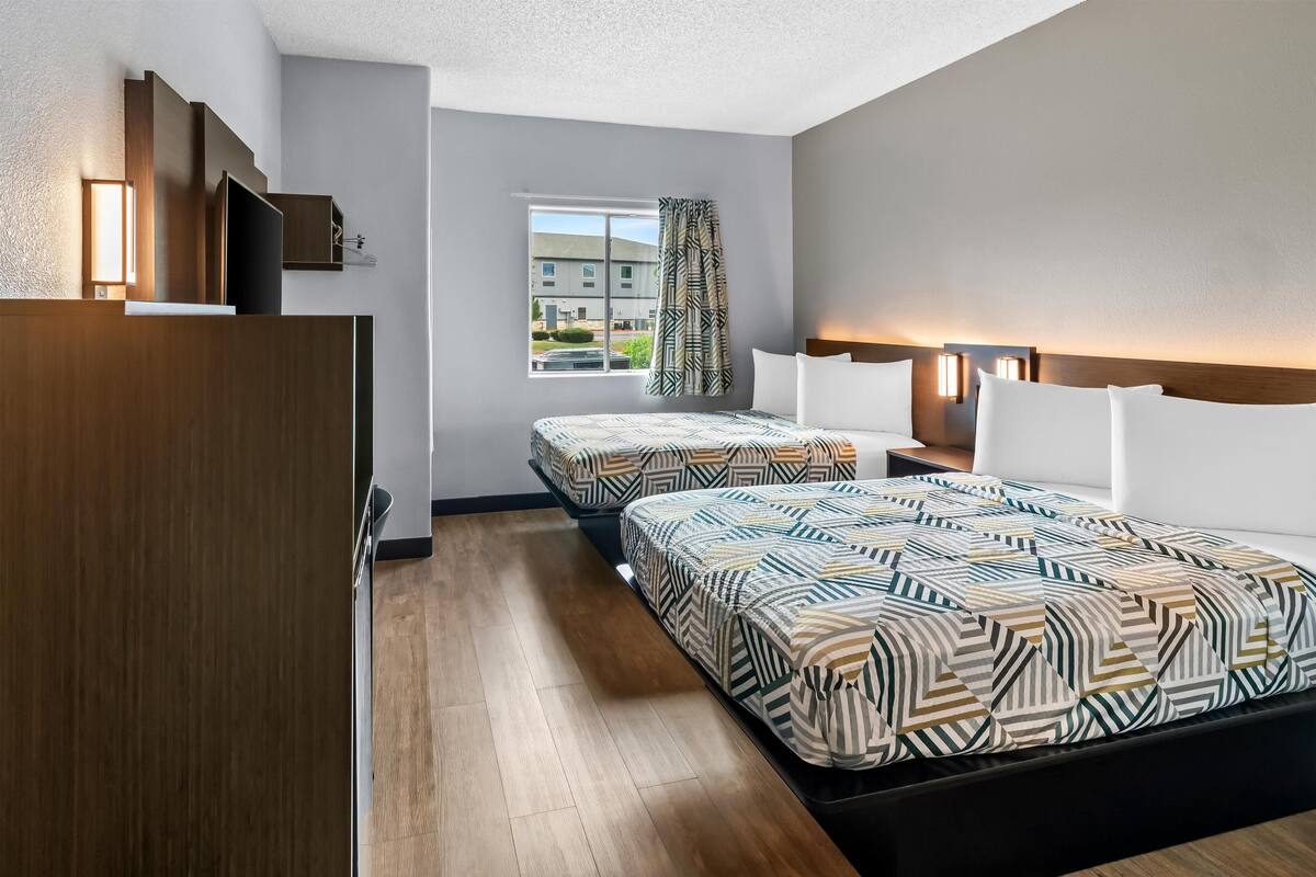 Hotellihuone, jossa on kaksi sänkyä, puinen vaatekaappi, televisio ja ikkuna, josta on näkymä rakennuksiin.