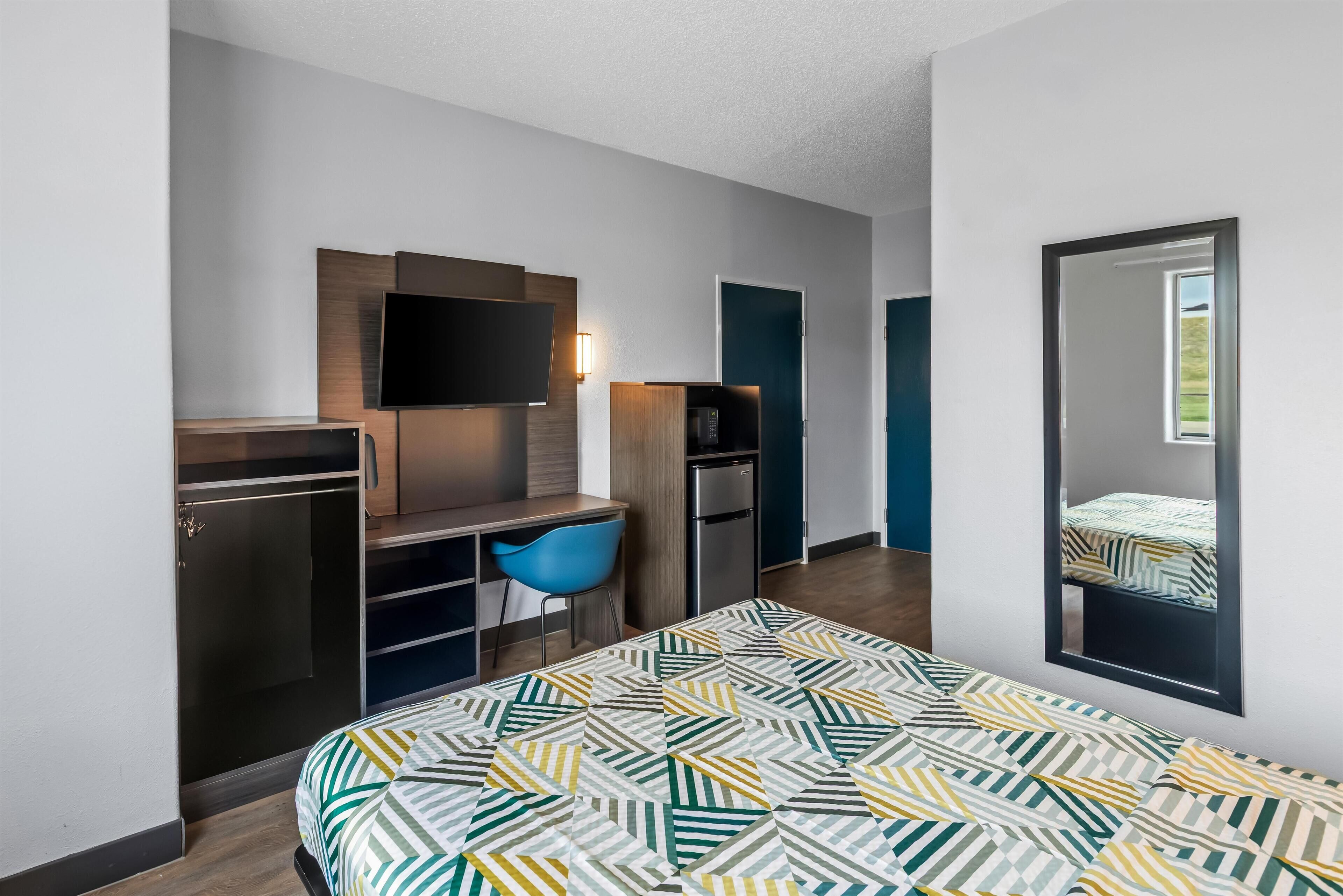 Una habitación de hotel moderna con cama, escritorio, silla, televisor y armario.