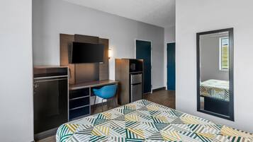 Una habitación de hotel moderna con cama, escritorio, silla, televisor y armario.
