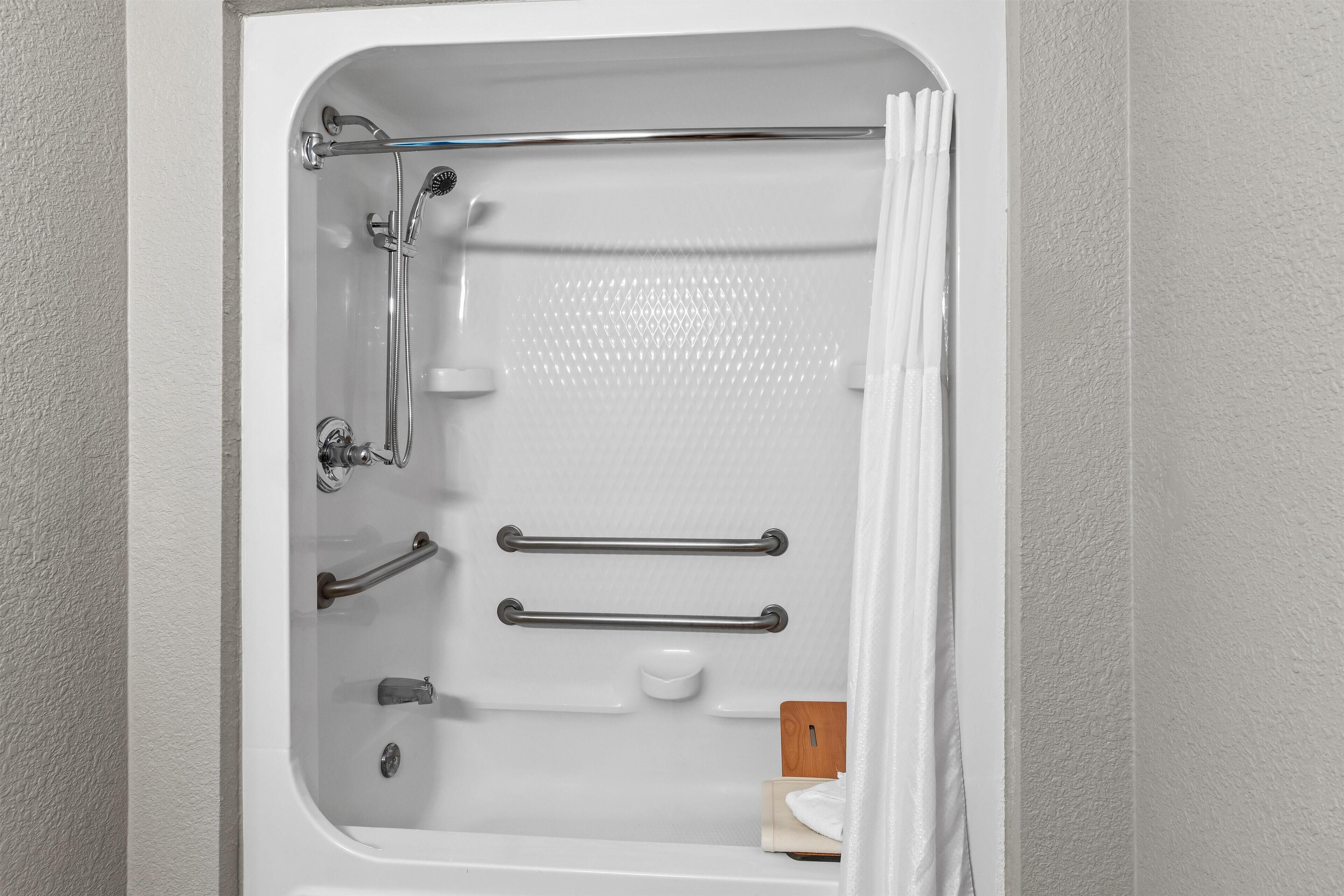 A white bathtub with chrome fixtures, a handheld showerhead, and two grab bars.