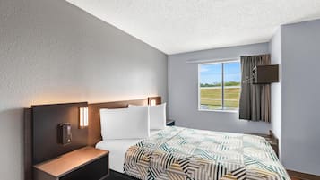 A modern hotel room with a large bed, a bedside table, a nightstand, a wall-mounted TV, and a window with a view of the outdoors.