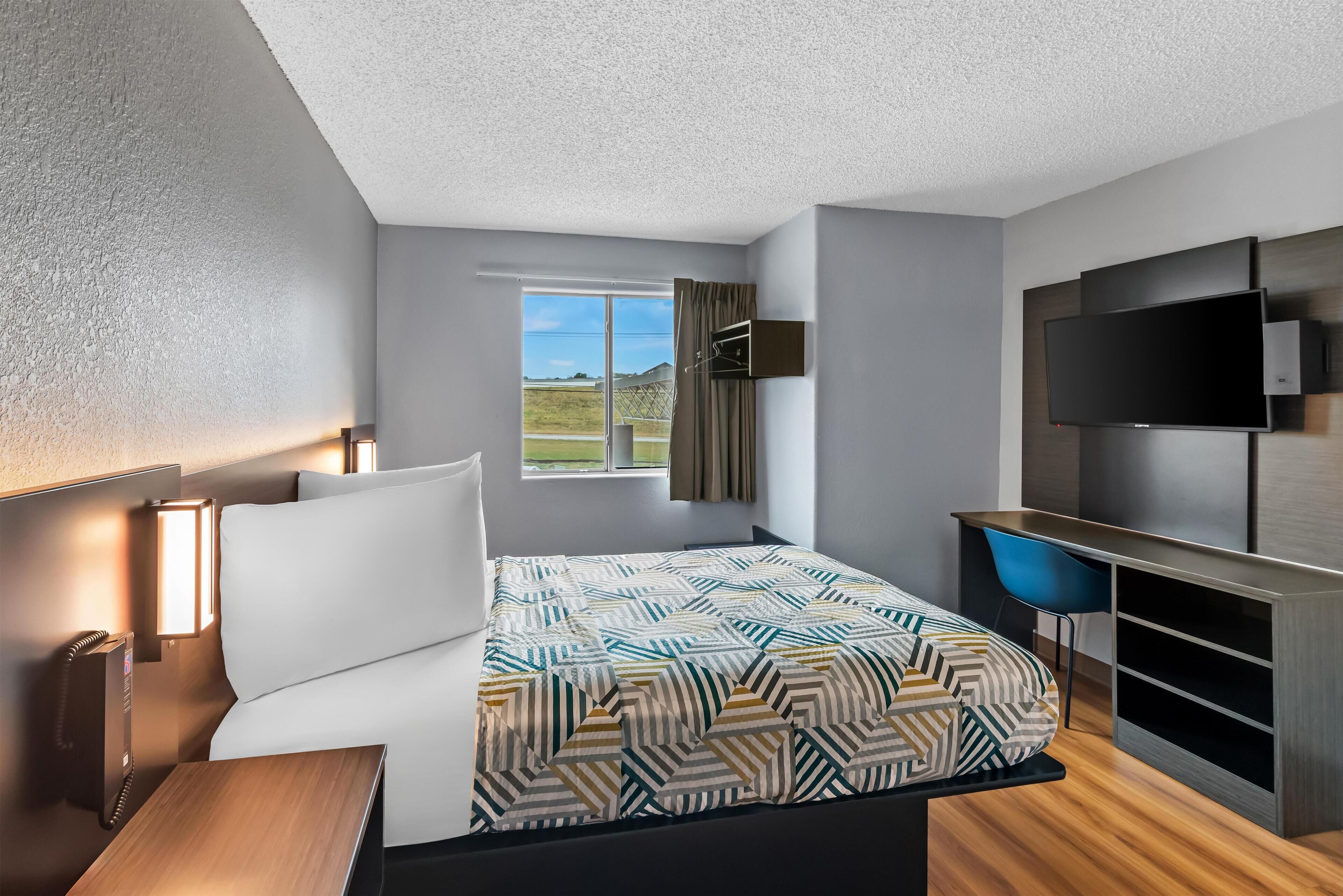 A modern hotel room with a bed, a desk, a flat-screen TV, and a window with a view of the outdoors.