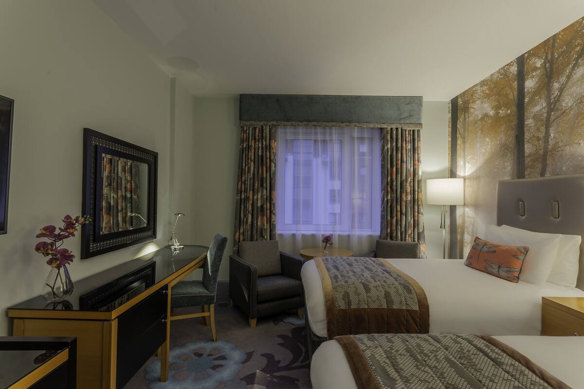 A hotel room with a bed, a desk, a chair, a lamp, and a painting on the wall.