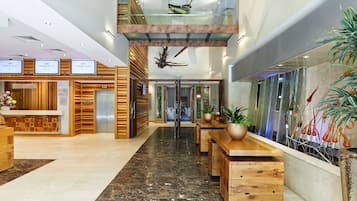 A hotel reception area with a modern design, featuring a reception desk, a staircase, and a seating area with wooden tables and chairs.