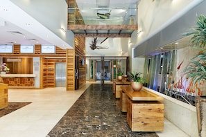 Een hotel receptie met een modern design, met een receptiebalie, een trap en een zithoek met houten tafels en stoelen.