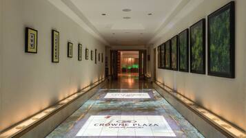 A corridor with framed artwork on the walls, a floor with a logo, and a view into a room with a green-lit reception area.