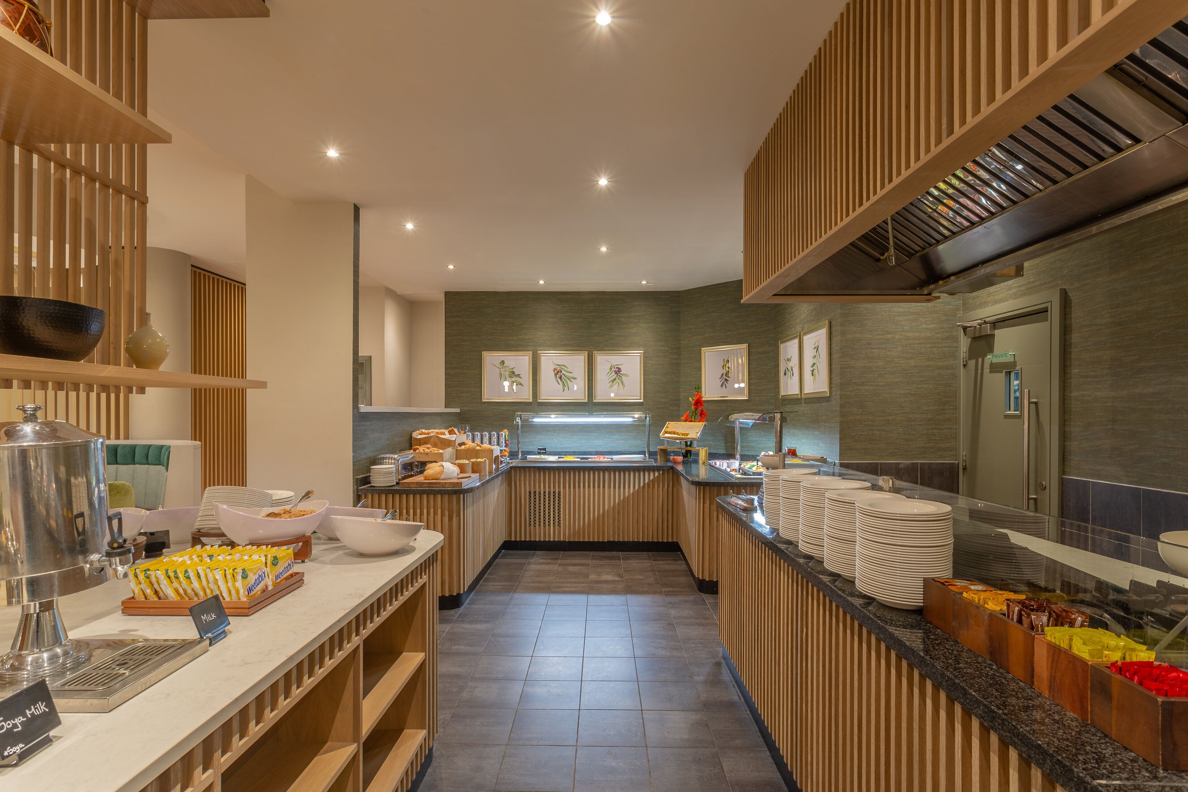 A modern hotel kitchen with buffet-style breakfast options, including bowls, plates, and a variety of food items.